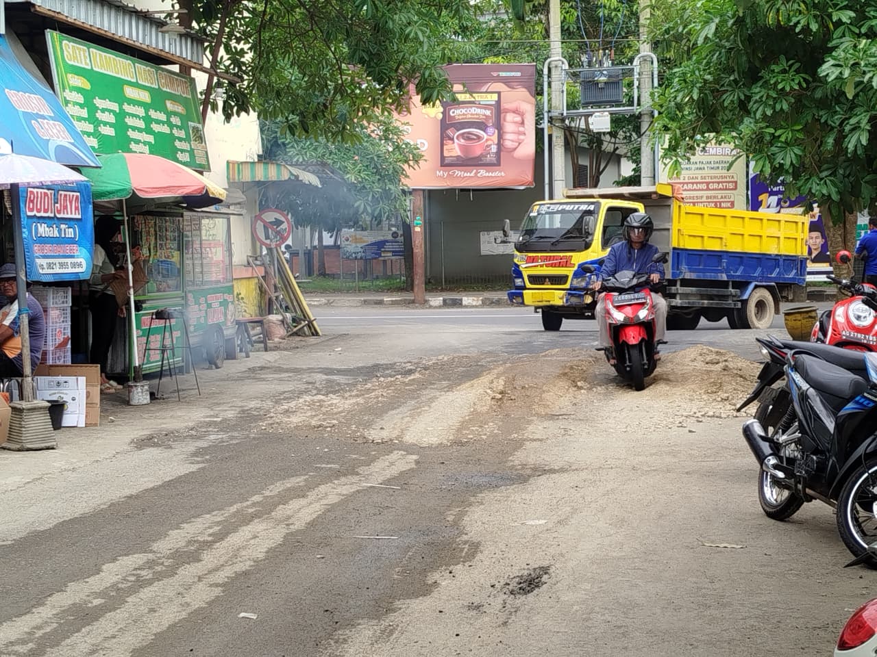 Kerusakan jalan di area Pasar Basah Trenggalek yang mengganggu pengendara akibat pengurukan proyek sekolah rakyat di lokasi.