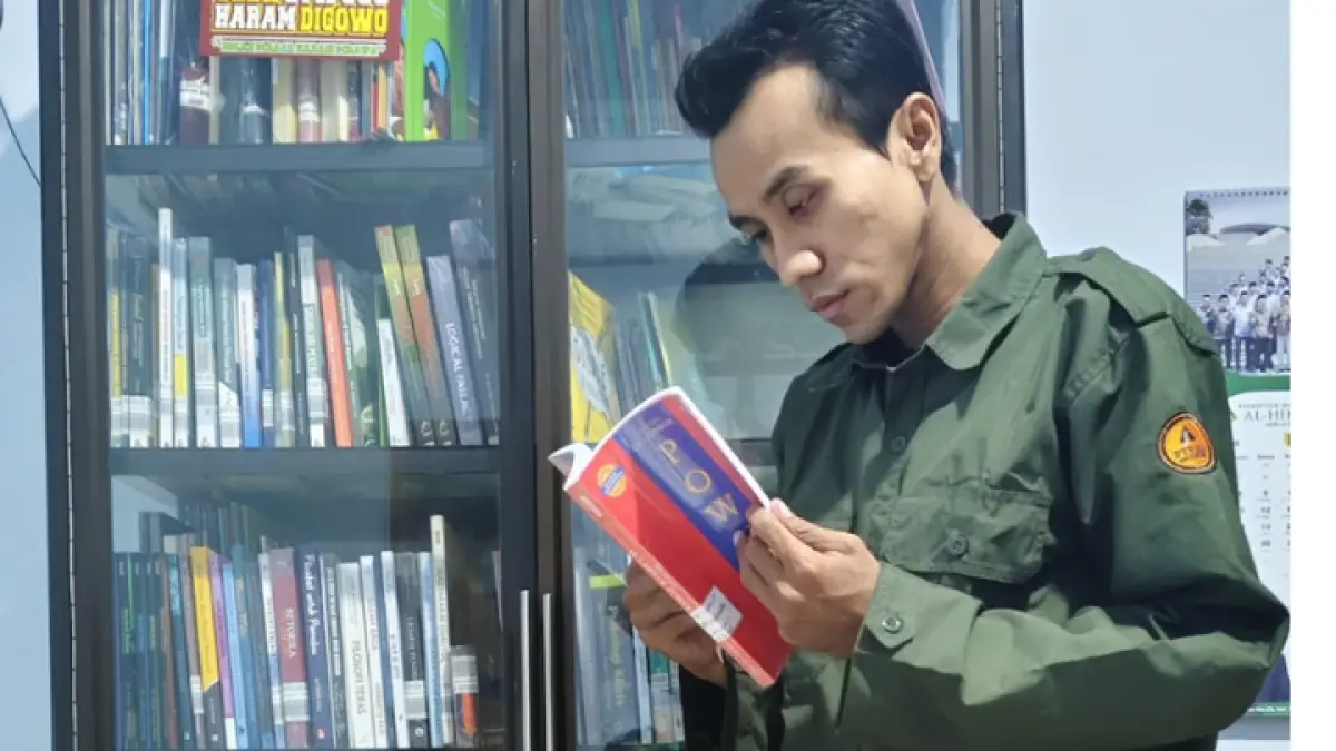JANGAN DIBAWA: Riyadu membaca salah satu buku koleksinya yang disiapkan kepada siapa yang mampir. (ZAKI JAZAI/ RADAR TRENGGALEK)