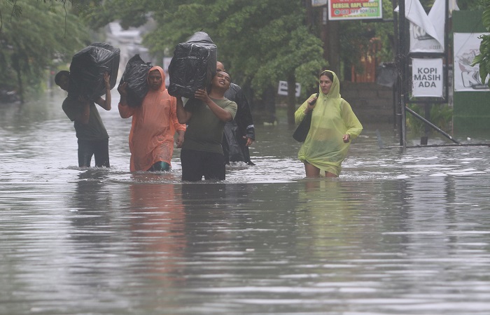 Wisatawan asing  meninggalkan tempat menginapnya dengan berjalan kaki melewati banjir di kawasan Jalan Dewi Sri Legian, Badung, Bali.