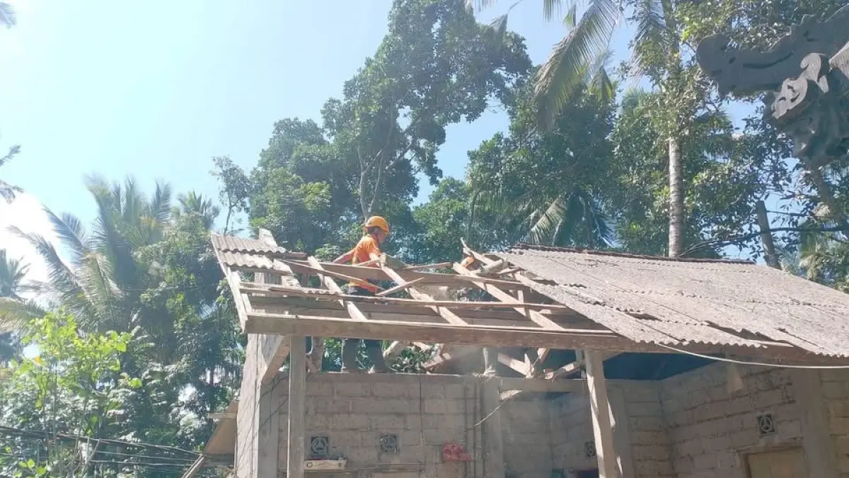 Petugas saat melakukan penanganan pohon tumbang yang menimpa rumah warga di Desa Nawakerti, Kecamatan Abang, Minggu (2/8). (Istimewa)