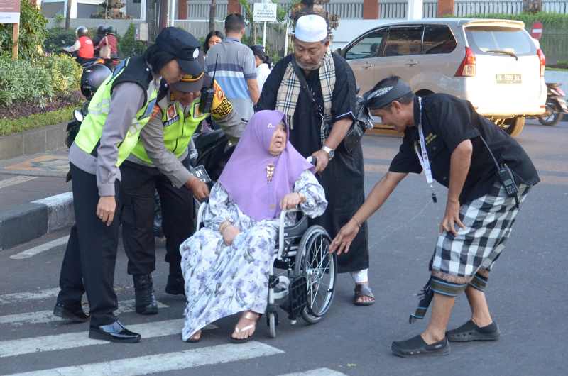 DIBANTU MENYEBERANG : Seorang ibu dengan kursi roda dibantu menyeberang usai salat Id di Lapangan Lumintang, Denpasar.