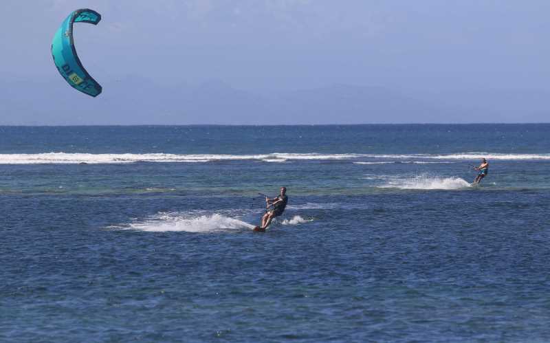 SENSASI ANGIN DAN OMBAK: Sejumlah wisatawan tampak menikmati ombak pantai Karang Sanur dengan main kite surfing