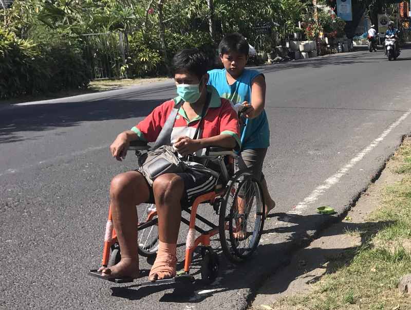 TAK ADA TROTOAR : Seorang bocah mendorong kursi roda di Jalan Hayam Wuruk, Denpasar, karena tidak ada trotoar, meskipun risikonya tidak aman. [miftahuddin halim]