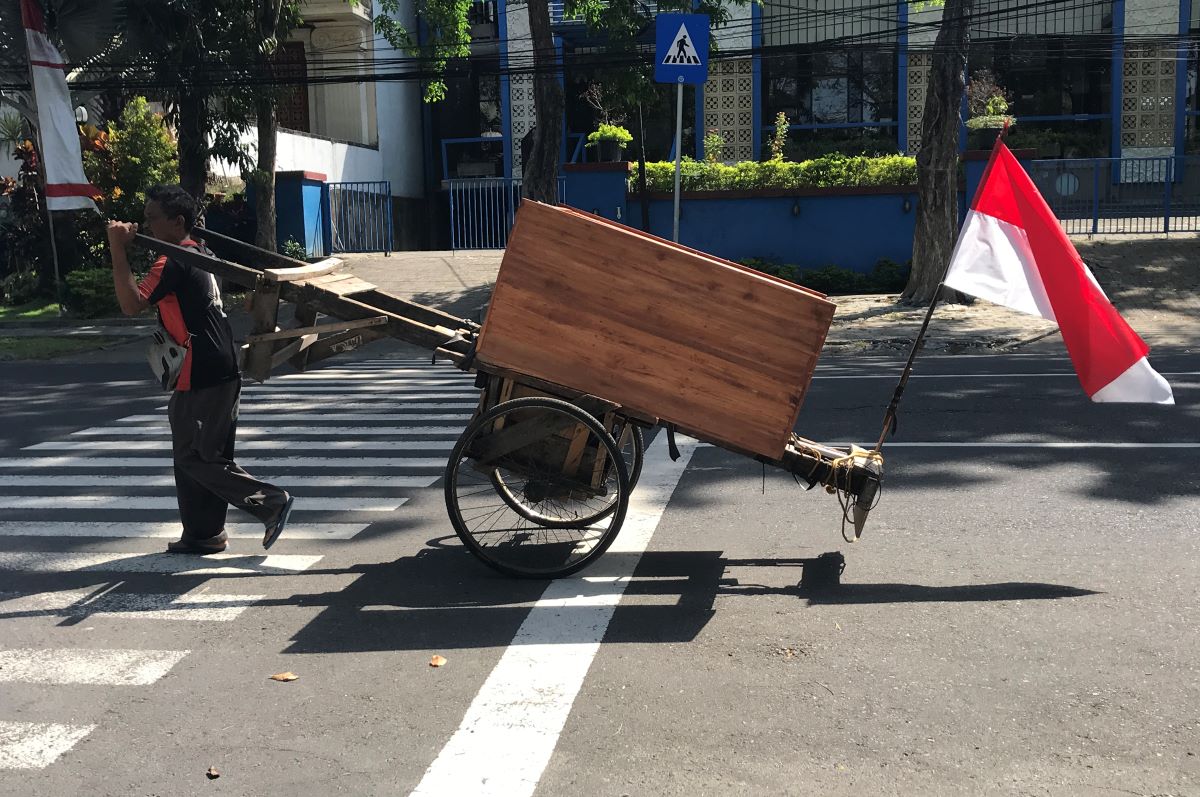 HARI MERDEKA: Seorang pedagang kursi keliling mendorong gerobak dengan memasang bendera merah putih di jalan Muh. Yamin Denpasar beberapa hari lalu.