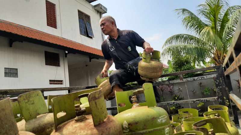 WASWAS STOK PASPASAN : Seorang agen saat menaikkan gas elpiji tiga kilogram ke atas mobilnya. (dewa ayu pitri arisanti/radar bali)