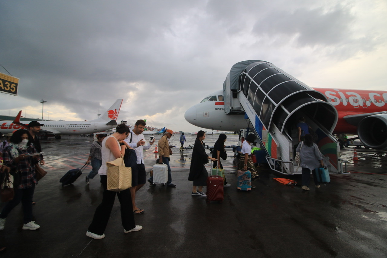 HUJAN LOKAL: Sejumlah penumpang berlari kecil menuju masuk pesawat karena mendung gelap dan mulai hujan  di area Bandara Internasional Ngurah Rai 22 April 2024