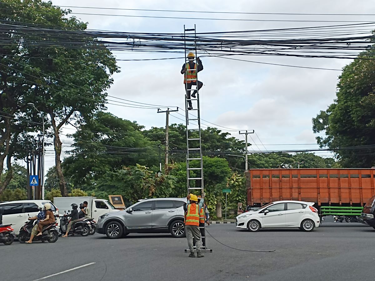 RUSAK ESTETIKA: Petugas tengah perbaiki kabel jaringan yang menjuntai mengganggu lalulintas di kota Denpasar.
