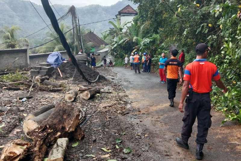 GOTONG ROYONG: Petugas dan warga bergotong royong melakukan penanganan pohon hingga tiang listrik yang tumbang menimpa akses jalan warga di Banjar Dinas Kaler, Desa Antiga,  Manggis. (Istimewa)
