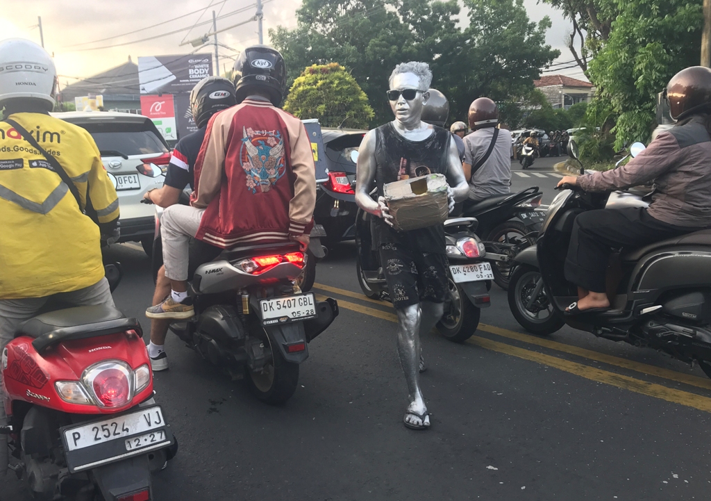 BERKELILING: Manusia silver sedang berkeliling membawa kotak sedekah ke sejumlah pengendara motor.