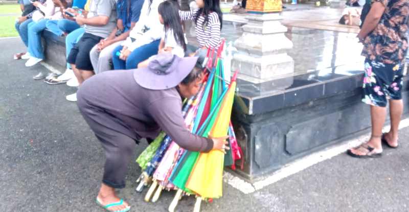 HUJAN ADALAH BERKAH : Ni Wayan Dariasih pekerja jasa sewa payung di kawasan DTW Ulun Danu Beratan, Bedugul Baturiti semringah bila turun hujan. (juliadi/radar bali)