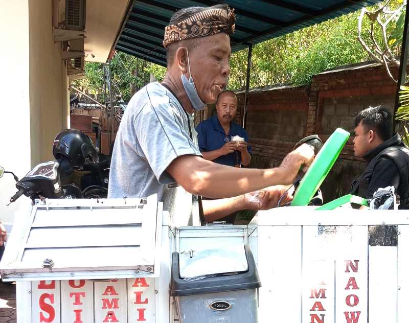 PEKERJA KERAS : Made Mardika saat meracik es roti buatannya di halaman Radio Gelora Gianyar. (ida bagus indra prasetia)