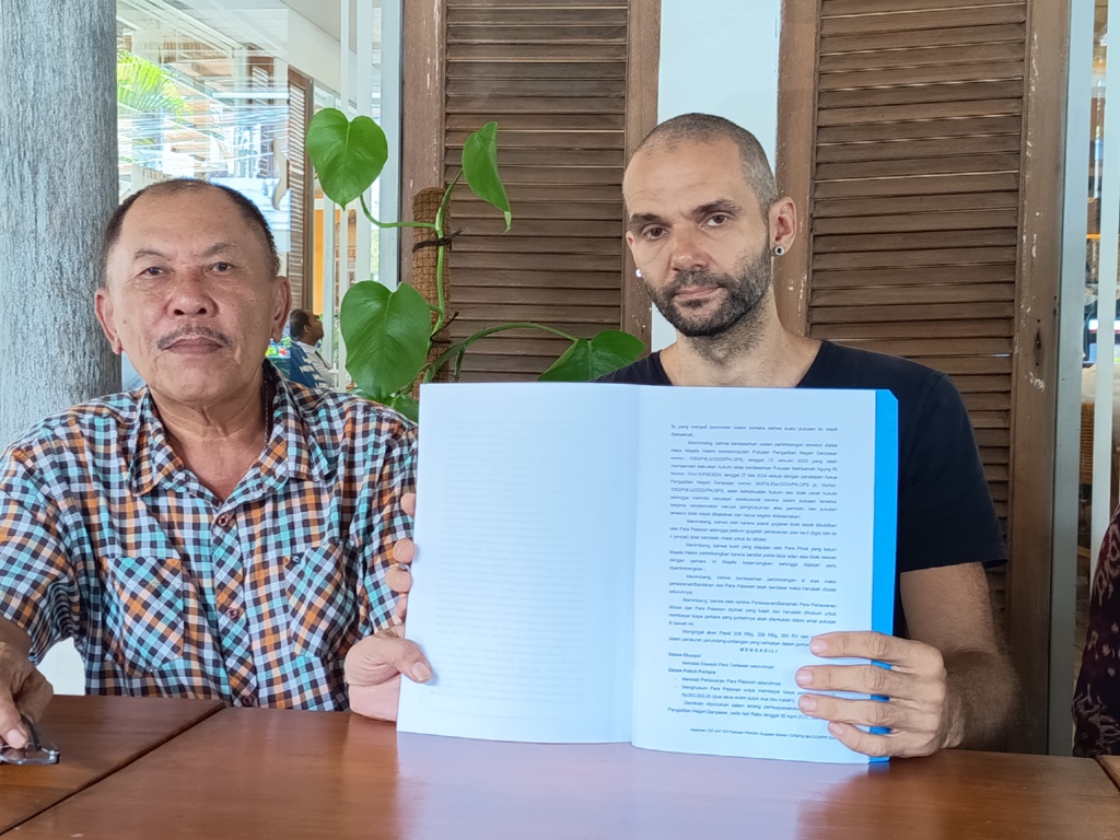 MINTA KEJELASAN: WN Ukraina, Sergio (kanan) menunjukkan putusan PN Denpasar yang memenangkan dirinya.