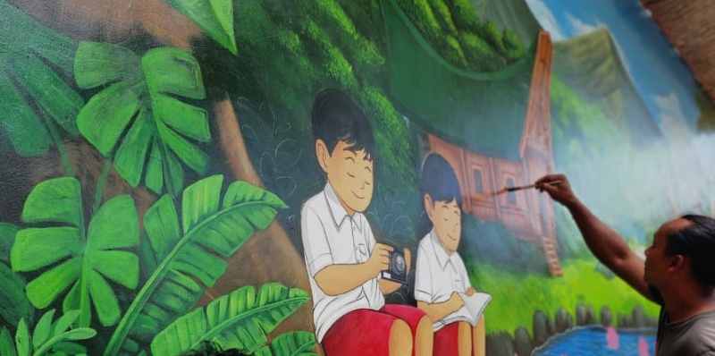 TUNTASKAN KARYANYA : I Gede Maha Putra Tengah menuntaskan karya muralnya. (ist)