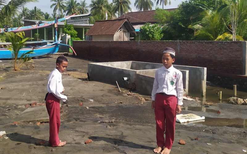 WASWAS OMBAK : Dua siswa depan MI Nurul Ikhlas Banjar Pebuahan yang terancam abrasi . (M.Basir)
