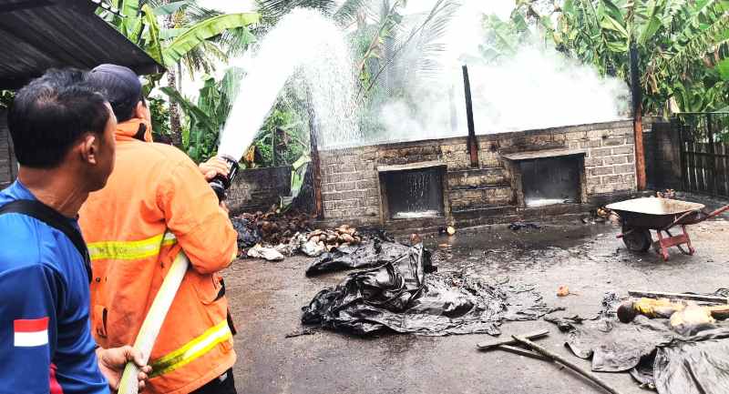 KERJA KERAS PADAMKAN API  : Petugas memadamkan sisa api yang membakar pengovenan kopra. (foto: Damkar Jembrana)