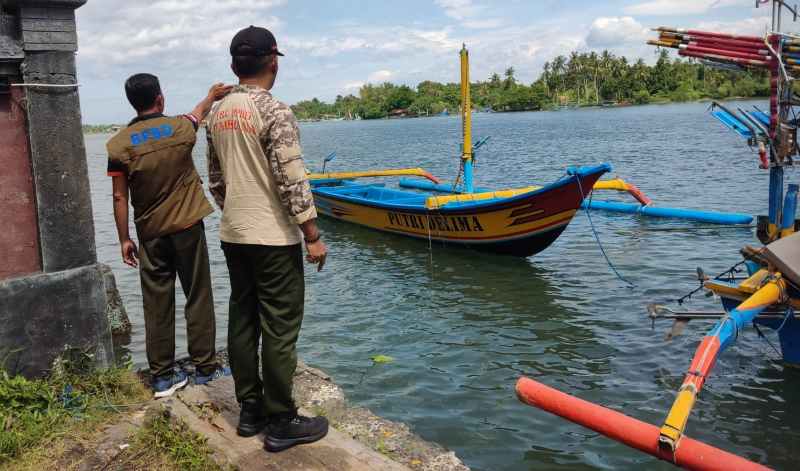 ANGIN KENCANG : Kalaksa BPBD Jembrana I putu Agus Artana Putra (pakai topi) saat melihat kondisi salah satu perahu nelayan yang sempat terbalik. (foto:BPBD Jembrana)