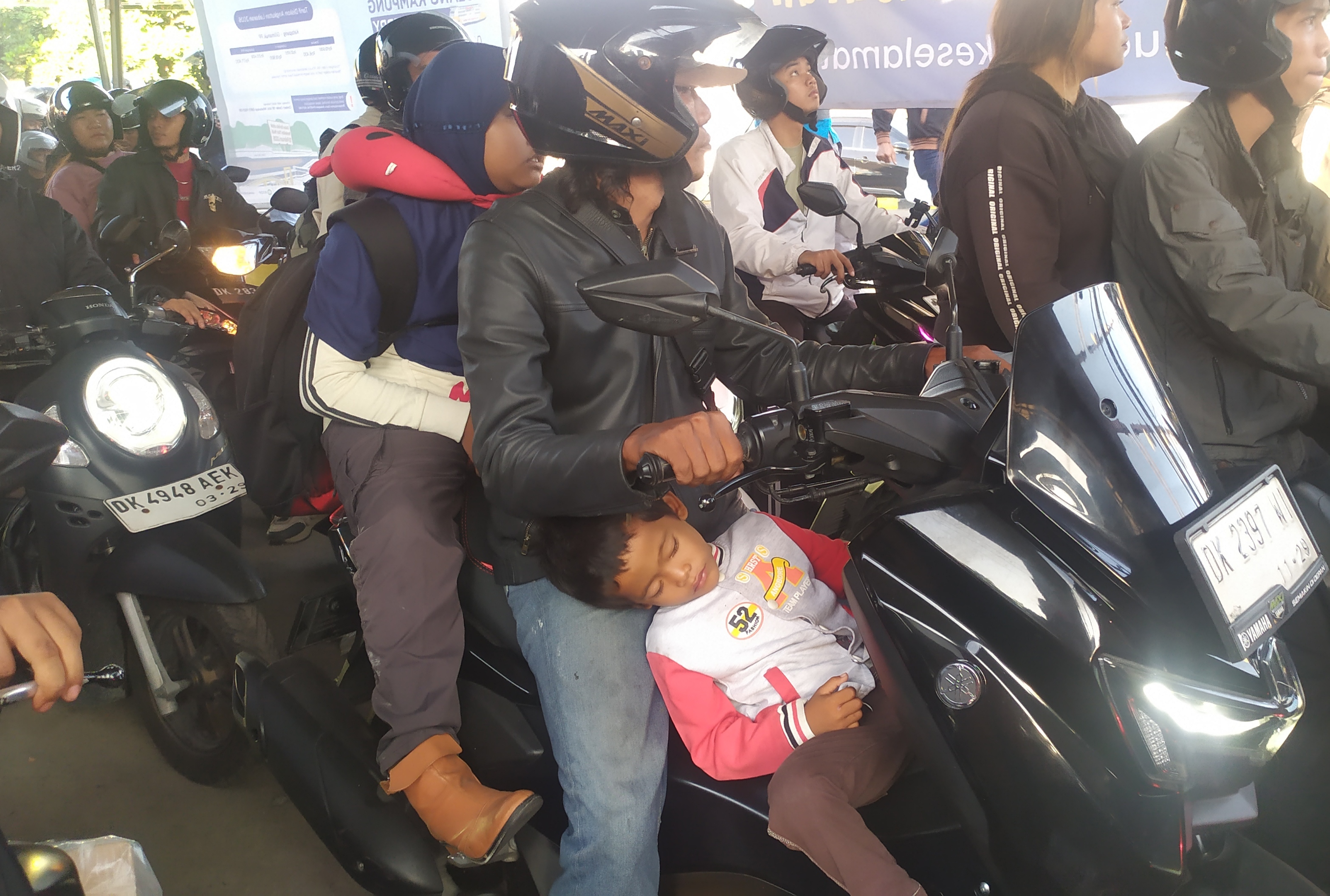MENGANTUK : Keluarga pemudik naik motor ini anaknya mengantuk di perjalanan. (M.Basir/Radar Bali)