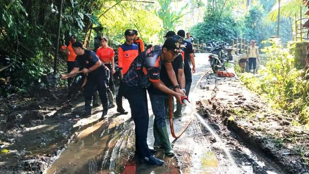 BERSIHKAN LUMPUR : Petugas BPBD Jembrana membersihkan jalan yang tertutup lumpur. ( foton : BPBD Jembrana)