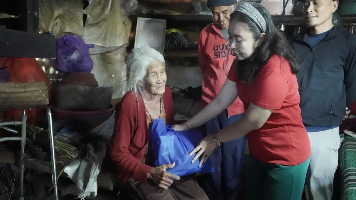 Nyonya Mas Parwata menyerahkan secara langsung paket sembako dan pakaian adat sembahyang kepada salah seorang lansia di Kecamatan Rendang, Minggu (2/8)