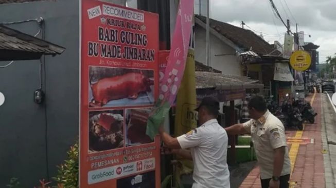 TURUN: Salah satu baliho Babi guling yang sedang diturunkan oleh aparat. (ist)
