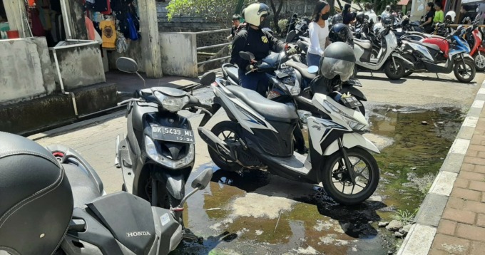 BAUNYA MENYENGAT : Air disertai bau busuk muncul dari aspal parkir selatan blok A Pasar Umum Semarapura. (foto:dewa ayu pitri arisanti/radar bali)