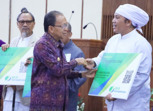 PERLUAS CAKUPAN UCJ: Gubernur Wayan Koster secara simbolis menyerahkan kartu peserta BPJS Ketenagakerjaan kepada ribuan rohaniwan lintas agama se-Bali di Wisma Sabha Utama, Jumat (12/5/2023).