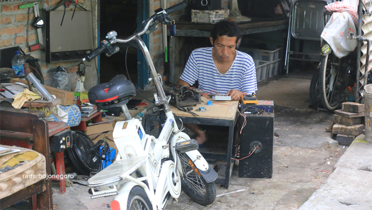 SERVIS MOTOR LISTRIK: Priyo Winarno sedang memperbaiki salah satu motor listrik di bengkelnya. Saat banjir kewalahan garapan. (WAHYU DHANI ALFIANSYAH/RADAR BOJONEGORO)
