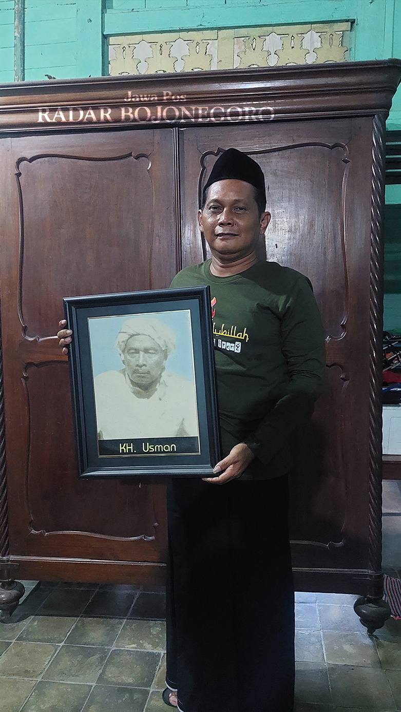 PENERUS: Kiai Anief sedang memegang foto kakeknya Kiai Usman. Di belakang tampak sebuah lemari digunakan menyimpan kitab-kitab Kiai Usman dahulu. (LUKMAN HAKIM/RADAR BLORA)