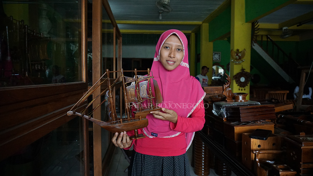 MINIATUR KAPAL LAUT: Frasiska, salah satu owner toko kerajinan sedang menunjukkan kerajinan miniatur kapal laut berbahan baku kayu jati. (HAKAM ALGHIFARI/RADAR BOJONEGORO)