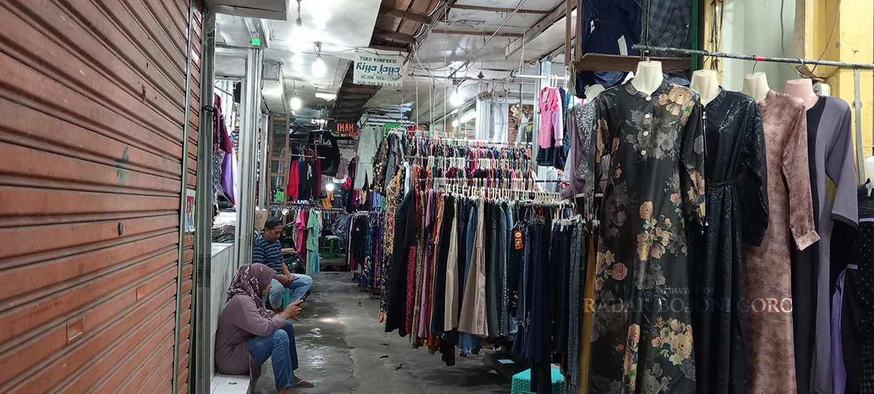 BERMAIN HP: Pedagang pakaian di Pasar Kota Bojonegoro santai bermain HP saat menjaga dagangannya, semakin hari makin sepi pembeli. (YANA DWI KURNIYA WATI/RADAR BOJONEGORO)