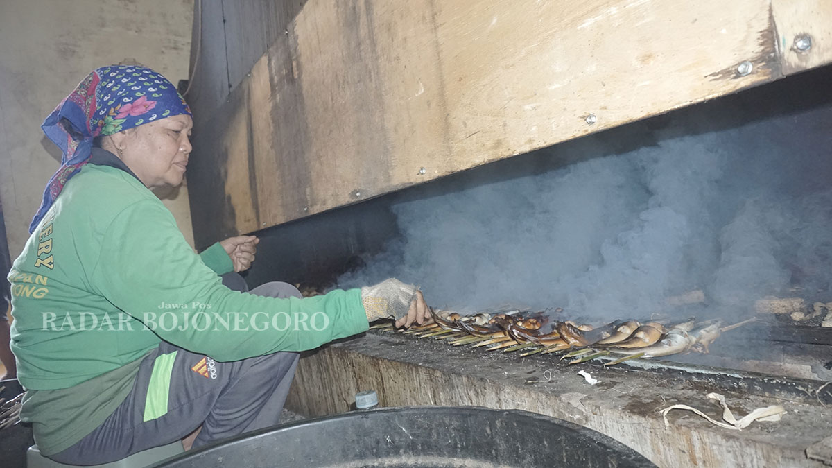 PENGASAPAN: Seorang perempuan paro baya sedang fokus memanggang ikan lele dengan teknik pengasapan. (HAKAM ALGHIVARI/RADAR BOJONEGORO)