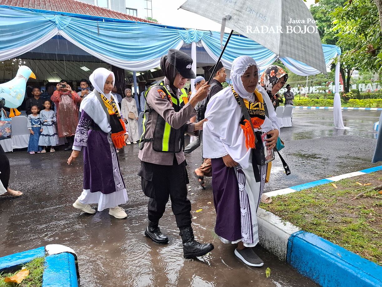 HUJAN: Polisi wanita membanti dengan memayungi CJH dari hujan saat di Pendapa Malowopati Bojonegoro. (DEWI SAFITRI/RADAR BOJONEGORO)