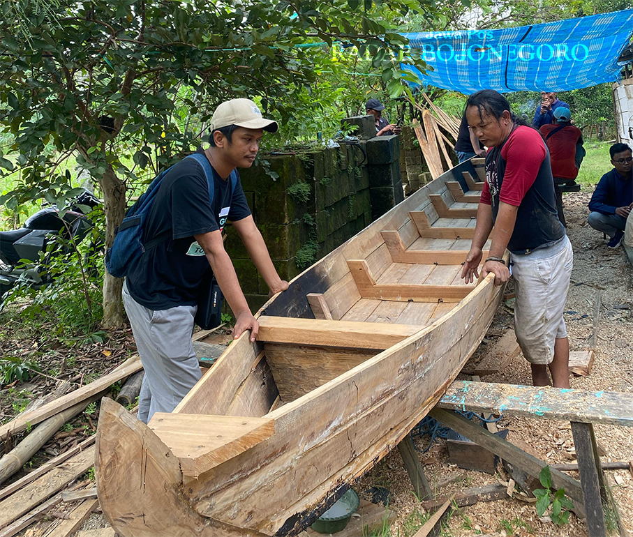 TETAP EKSIS: Salah satu pengunjung melihat langsung proses pembuatan perahu karya Muhsin. (LUKMAN HAKIM/RADAR BOJONEGORO)