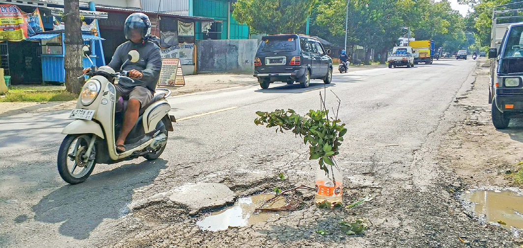MEMBAYAKAN: Salah satu titik jalan nasional yang berlubang diberi tanda galon dan ranting pohon.