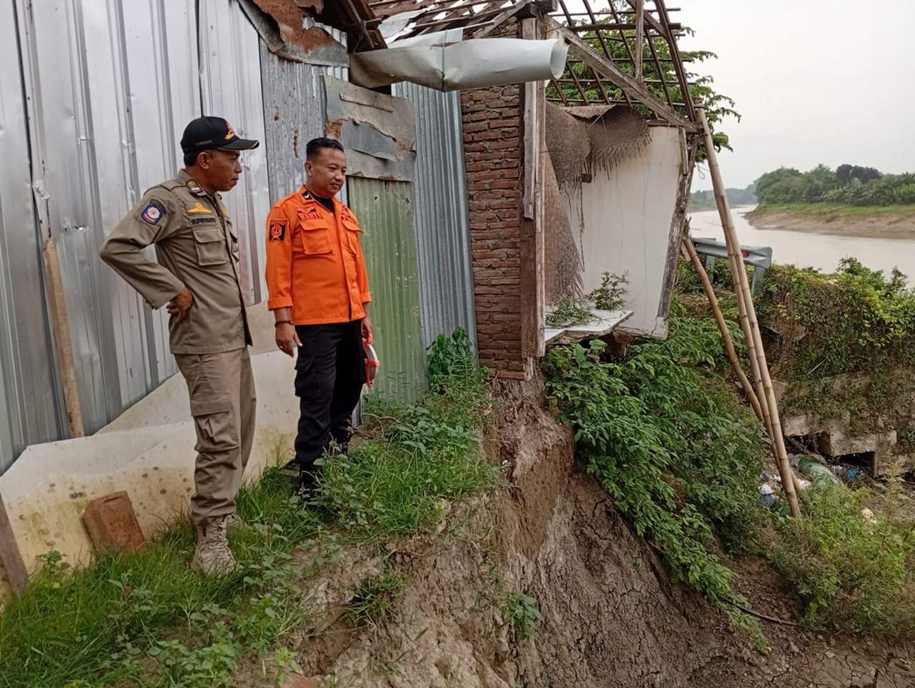 TERGERUS: Petugas saat memantau rumah warga yang terancam longsor karena tergerus arus sungai.