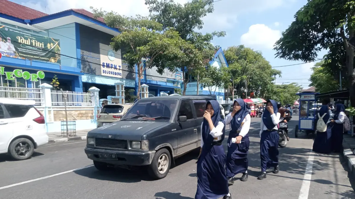 DIBATASI: Siswa menyeberang jalan dengan memegang HP, selama jam pelajaran sekolah, siswa wajib mengumpulkan, agar fokus pada pelajaran. (M.IRVAN RAMADHON/RADAR BOJONEGORO)
