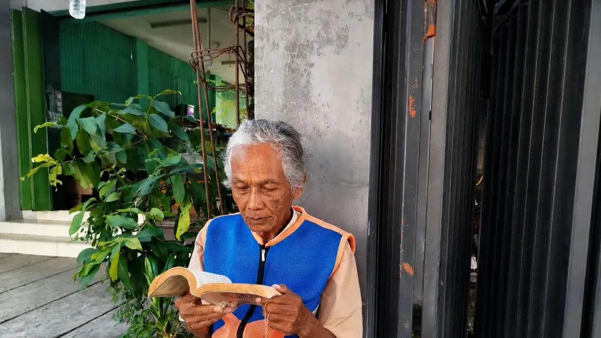 SERIUS: Suyono sedang asyik membaca buku di tengah kekosongan menjadi tukang parkir. (ACHMAD SYAEROYZI/RDR.BJN)