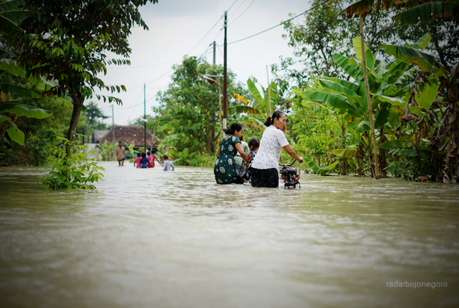 TEROBOS AIR: Ibu-ibu melintas di jalan Desa Kabunan. Banjir luapan Kali Pacal ini lebih 50 cm. (ALLIF ABDILLAH FAJAR MG-2/RDR.BJN)