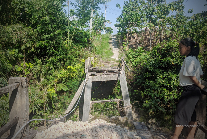 TERISOLIR: Jembatan terputus di Dusun Belah, Desa Turi, Kecamatan Tambakrejo. Jembatan rusak sejak November lalu. Ada warga 27 rumah terdampak. Tampak seorang nenek melintas menyeberangi sungai, kemarin (8/6). (DHANI WAHYU ALFIANSYAH/RDR.BJN)