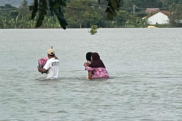 Warga Desa Merak, Kecamatan Dempet menerjang lautan air untuk mengungsi sembari menggendong orang tuanya (Wahib Pribadi/Jawa Pos Radar Semarang)