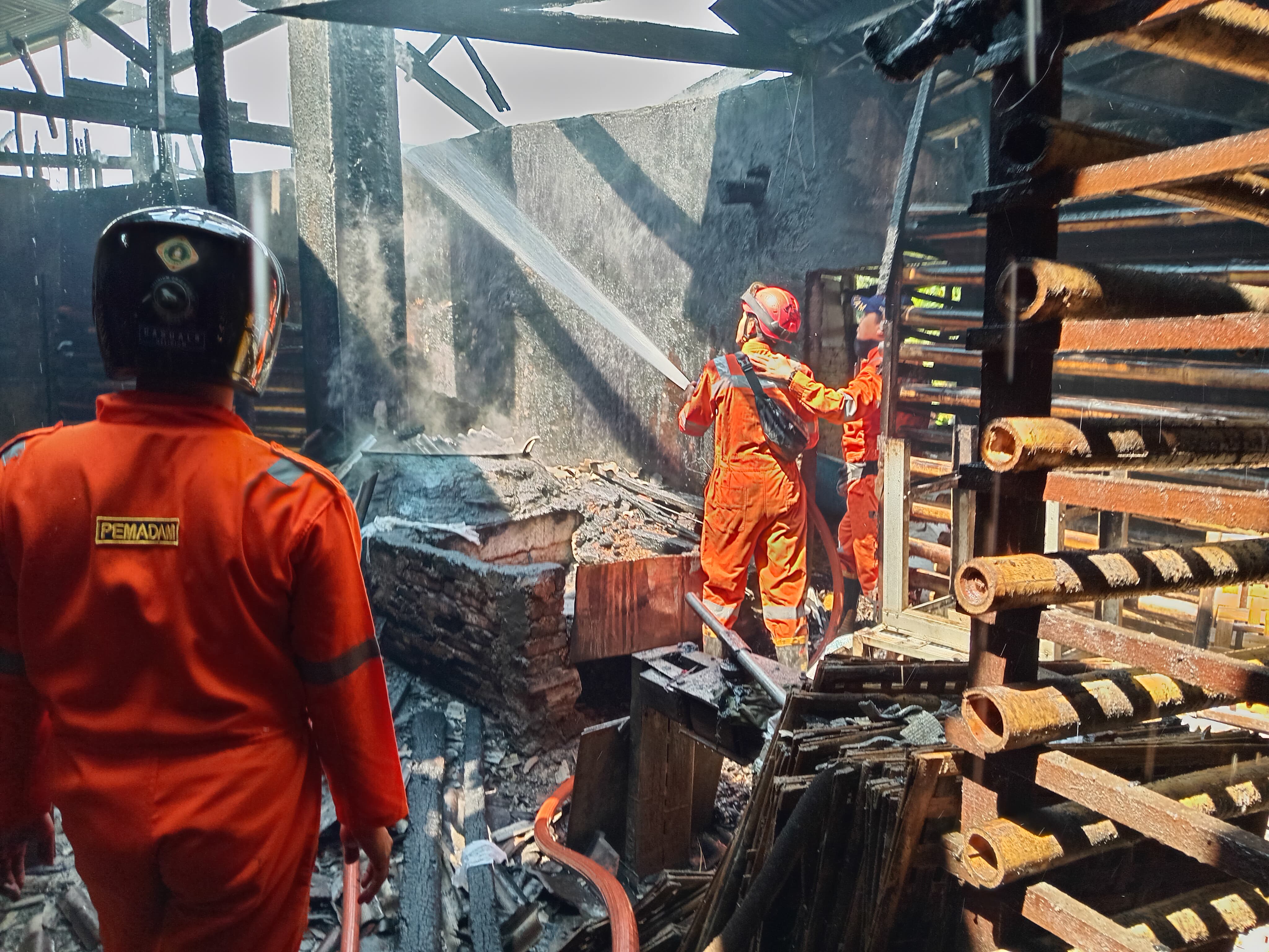 Petugas damkar tengah melakukan pendinginan di dalam pabrik tahu yang terbakar