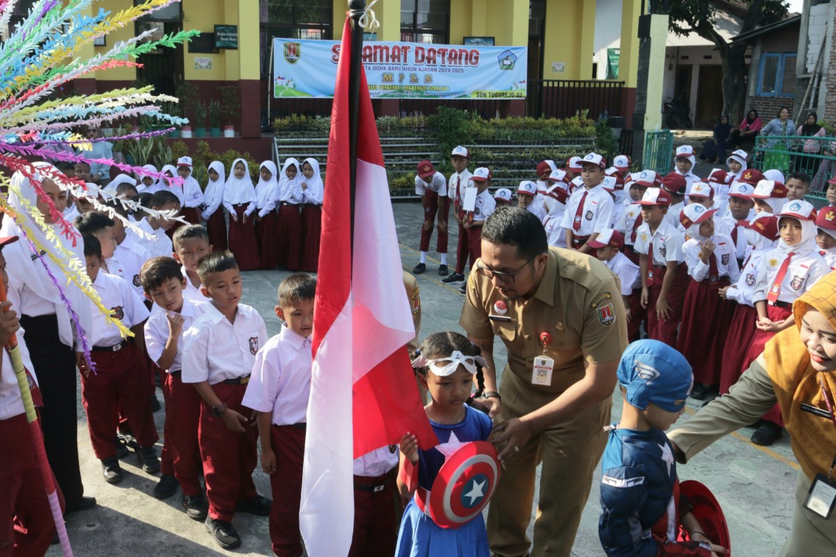 Siswa baru SDN Tugurejo 02, mengenakan kostum superhero dan mencium bendera pada hari pertama masuk sekolah, Senin (22/7/2024).&nbsp;NUR CHAMIM/JAWA POS RADAR SEMARANG