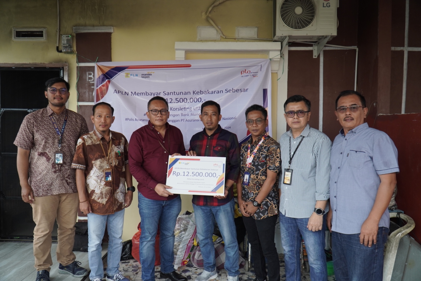 *Caption:* Penerima Santunan Kebakaran, Syahril (tengah, kemeja kotak-kotak merah), diapit Distribution Head IX Bank Mandiri Taspen, Tumbur Tobing (kiri, kemeja merah), dan Kepala Cabang APLN, Yusran