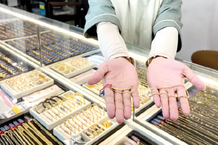 Seorang karyawan toko emas menunjukkan emas perhiasan berupa kalung emas.