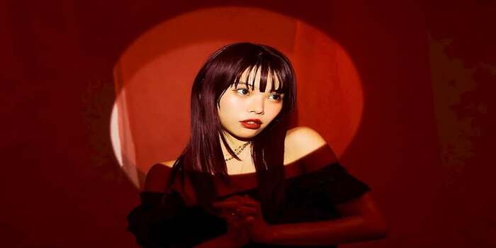 Tangkapan layar dari akun Instagram ainatheend_official, menampilkan sosok cantik yang berdiri dalam sorotan cahaya merah dengan ekspresi tajam dan gaya artistik. Ia mengenakan busana gelap.
