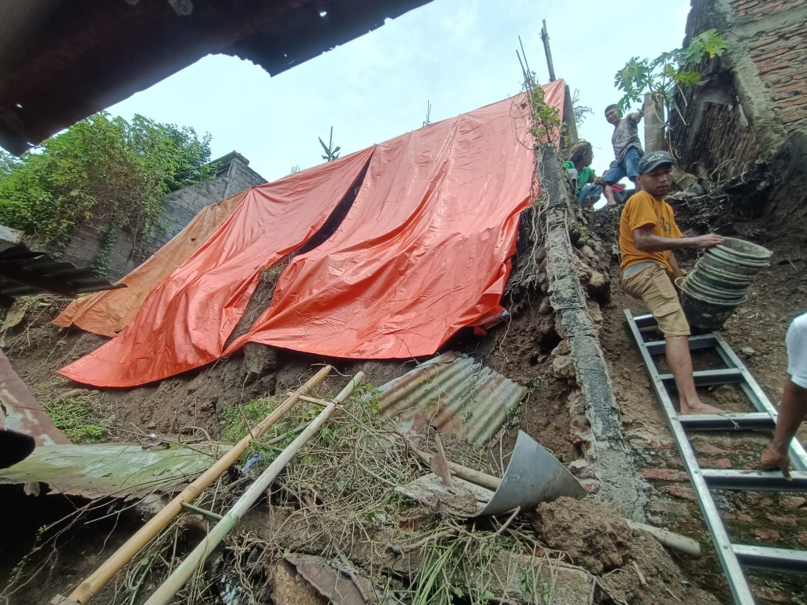material longsor berupa tanah bercampur pecahan pondasi menumpuk di halaman rumah warga dan menutup sebagian akses jalan kampung.