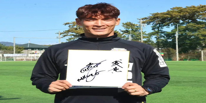 Manajer J2 Fujieda, Makino Tomoaki, tersenyum sambil memegang papan bertanda tangan di lapangan latihan, menunjukkan antusiasmenya menyambut musim baru J.League.