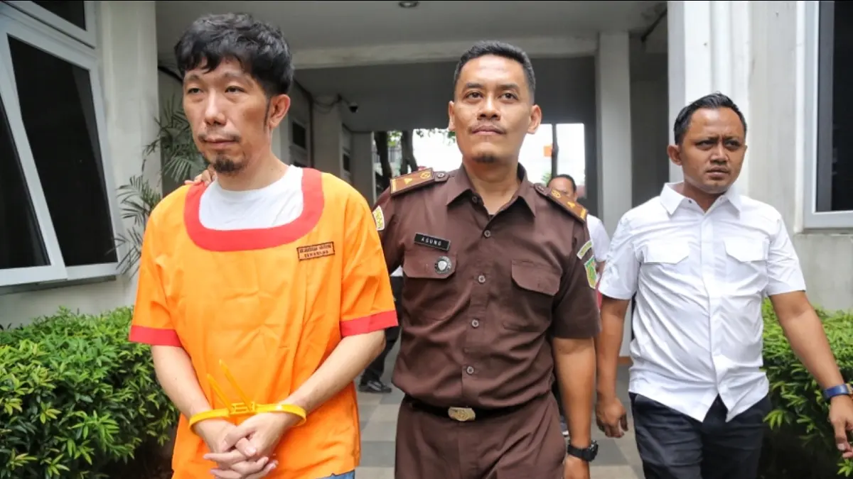 Tersangka mengenakan baju tahanan kejaksaan dengan tangan terikat saat proses pelimpahan Senin (22/6/2026)