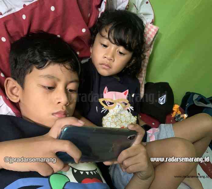Dua orang anak tengah asyik bermain handphone. Mereka akan berhenti bermain ketika alarm berbunyi. (Rizal Kurniawan/Jawa Pos Radar Semarang)