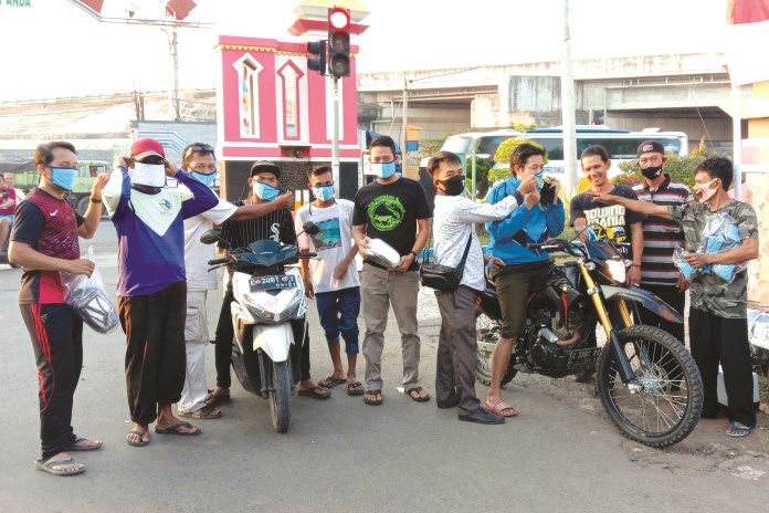 Ketua Bumdes Cokrokembang dan Ketua Karang Taruna Mandala Karya Desa Mentosari Kecamatan Gringsing memakaikan masker kepada warga yang melintas. (Riyan Fadli/Jawa Pos Radar Semarang)